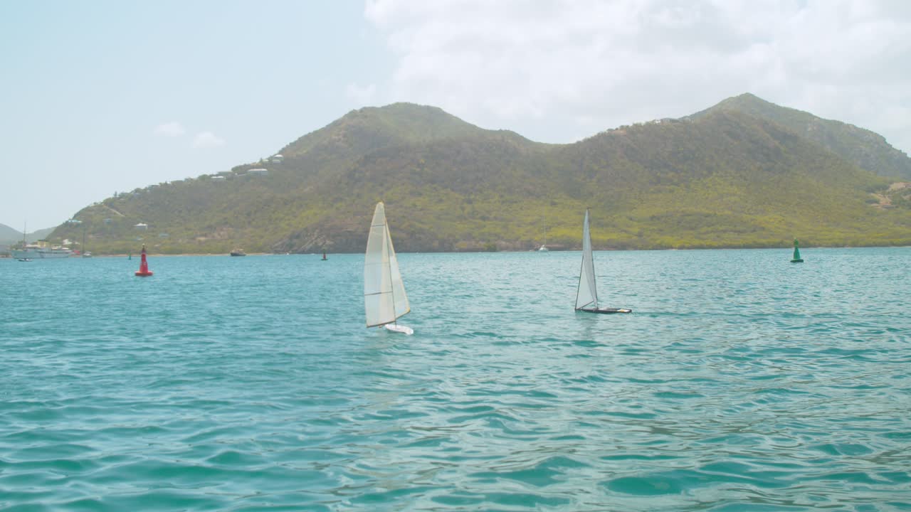 two model RC boats racing on open water with green mountains in the background