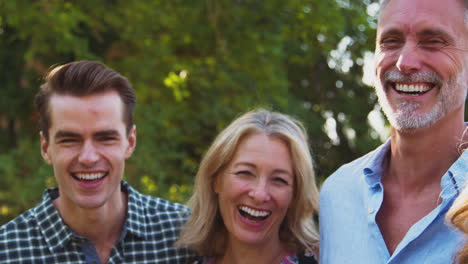 portrait of multi-generation family with adult offspring leaning on fence walking in countryside