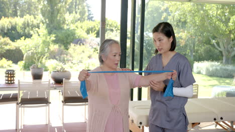 senior asian woman using resistance band with physical therapist in home session