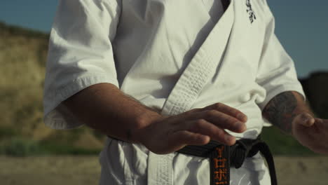 black belt fighter training hands exercises practicing karate ion beach closeup.