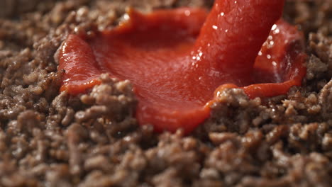 tomato sauce pouring onto the sizzling ground beef in the skillet - preparing sauce for spaghetti bolognese in macro and slow motion