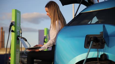 a business woman is charging an electric car and working with a laptop. modern cars with fast electric charging