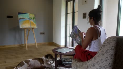 mujer lee en una habitación acogedora con perro y pintura
