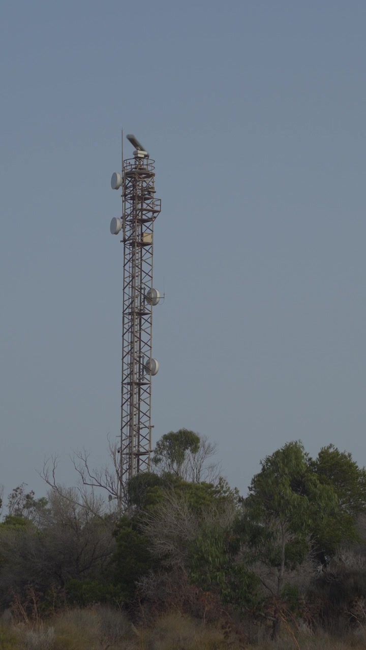 Inquadratura verticale statica di un'antenna radar marina che ruota su una torre di telecomunicazioni. Sfondo con paesaggio scenografico di colline costiere mediterranee. Ideale per progetti tecnologici e marittimi.