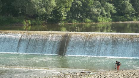 man recording nature sounds by the river with a dam behind