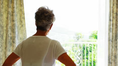 senior woman looking through a window in bedroom