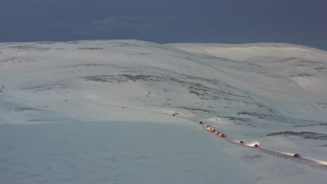 a convoy of cars driving on an icy road towards the nordkapp, norway during the midwinter solstice. high angle aerial shot