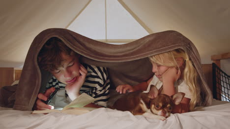 siblings reading and cozying up with a dog in a tent