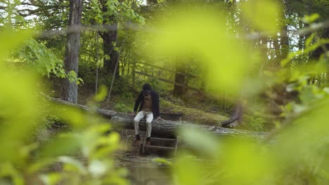 Looking-at-a-man-sitting-on-a-tree-trunk-bridge-through-the-leaves---slomo