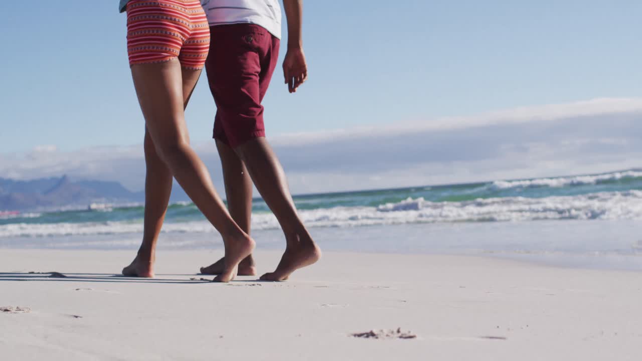 sección baja de una pareja afroamericana abrazándose y caminando por la playa