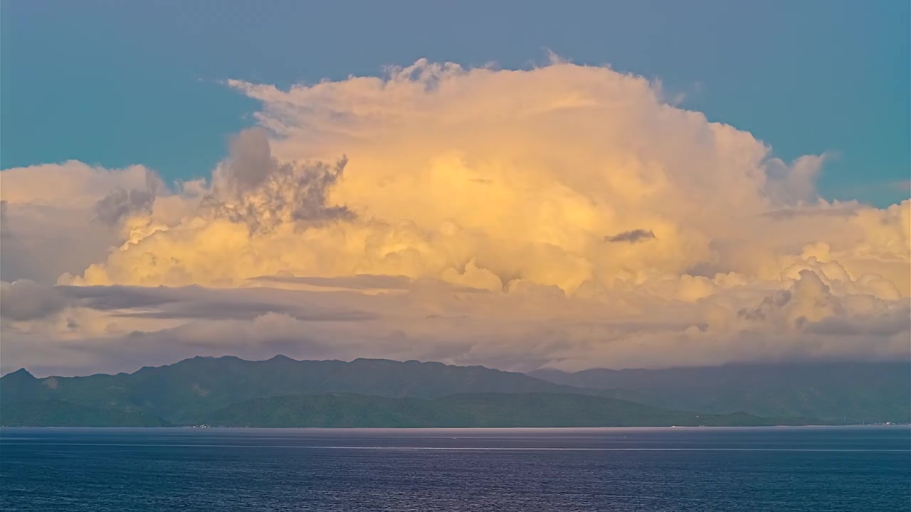 En dramatisk himmel med gyllene moln tornar upp sig över det lugna havet och avlägsna berg, vilket skapar ett fridfullt och majestätiskt landskap - Hyperlapse