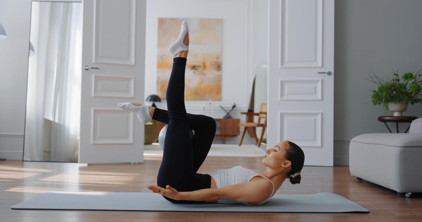 Giovane donna che esegue un esercizio di Pilates per il core con una piccola palla a casa