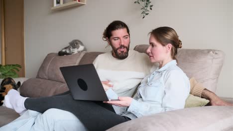 Couple laughing together while using a laptop on the couch at home