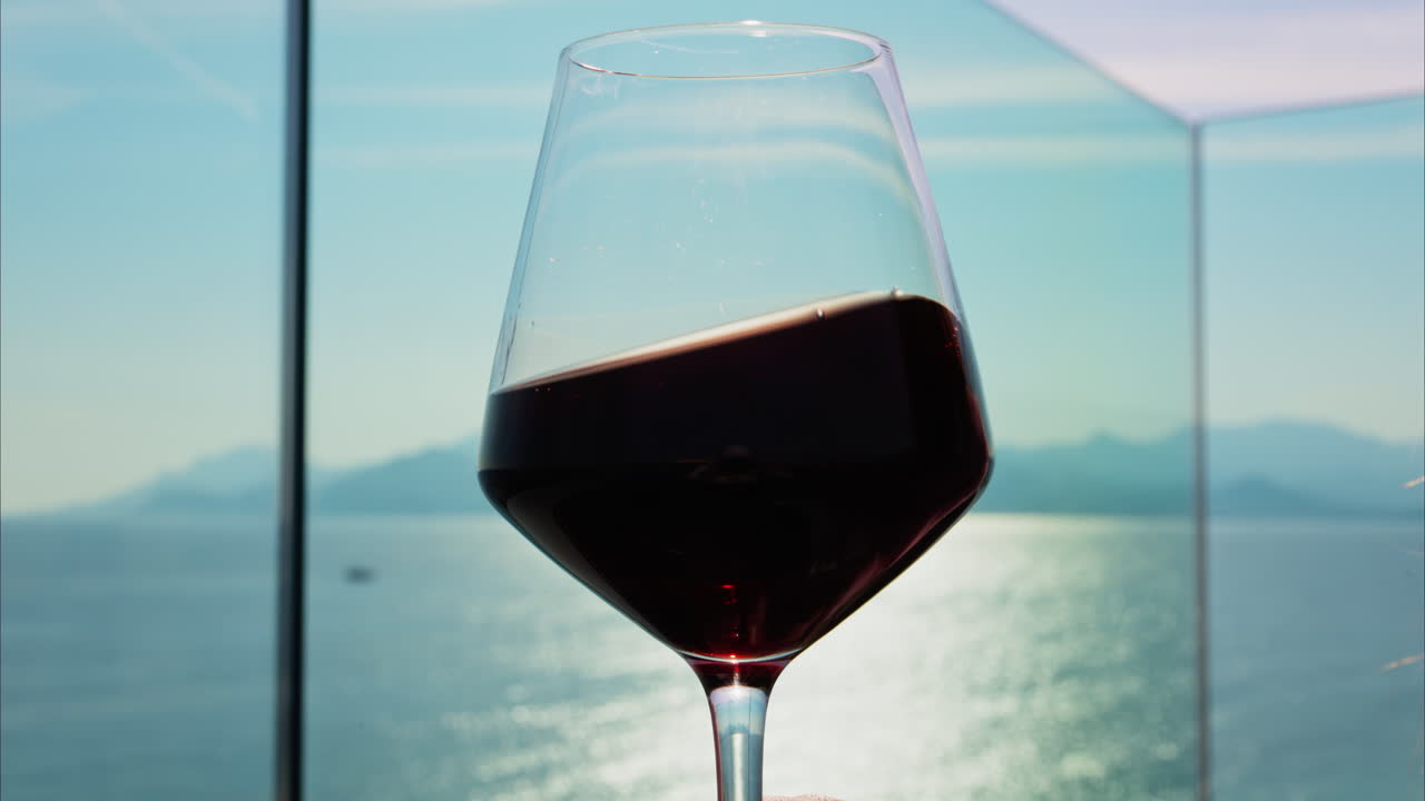Close up of a glass of red wine on a table at a terrace with a sea view