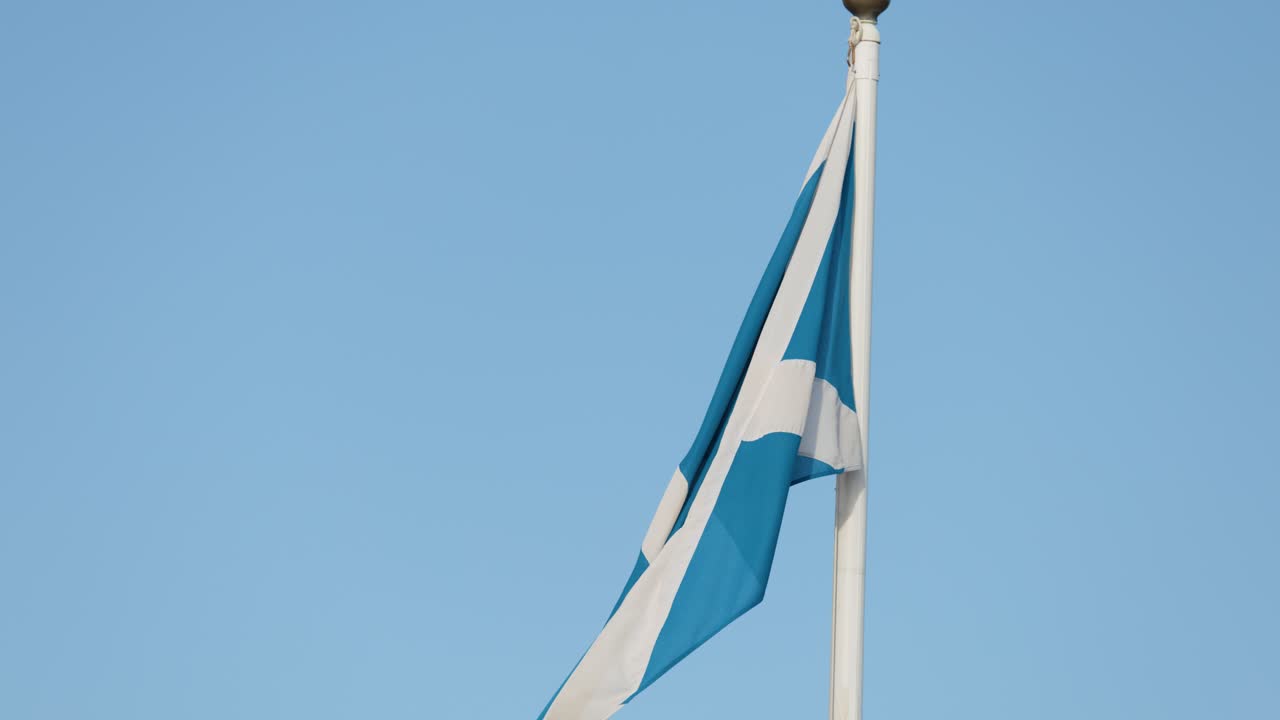 Scottish flag waves in gentle breeze, static camera, bright daylight, clear blue sky background