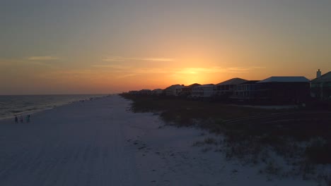 a drone shot of the beach at sunset with a quaint little town in the background