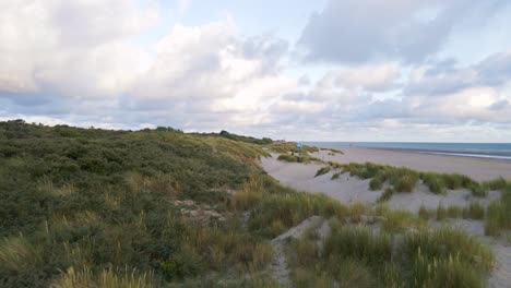 Slow-forward-flight-over-dune-landscape-with-sandy-each-and-seascape