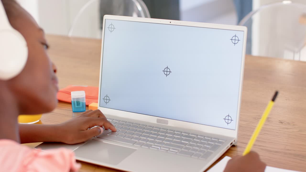 Med en bærbar computer, der viser sigtekors, skifter barnet mellem trackpad og blyantnoter ved bordet for at arbejde.