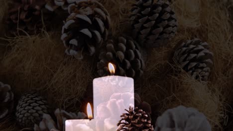 Animation-of-lit-candles-and-christmas-decorations-with-pine-cones-in-background