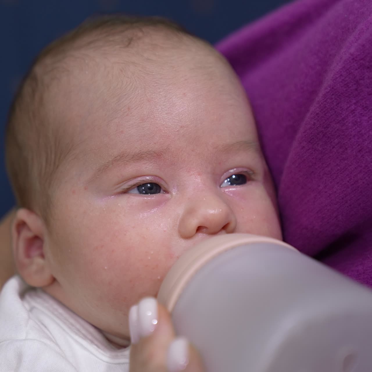 Cute infant suckling milk slowly from a bottle. Baby closing eyes and falling asleep while eating. Kid in mommy's hands close up