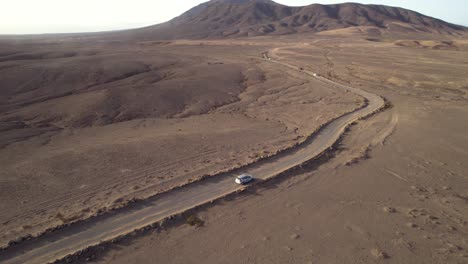 Toma-Aérea-De-Un-Coche-Conduciendo-Por-Una-Carretera-Polvorienta-En-Un-Día-Soleado