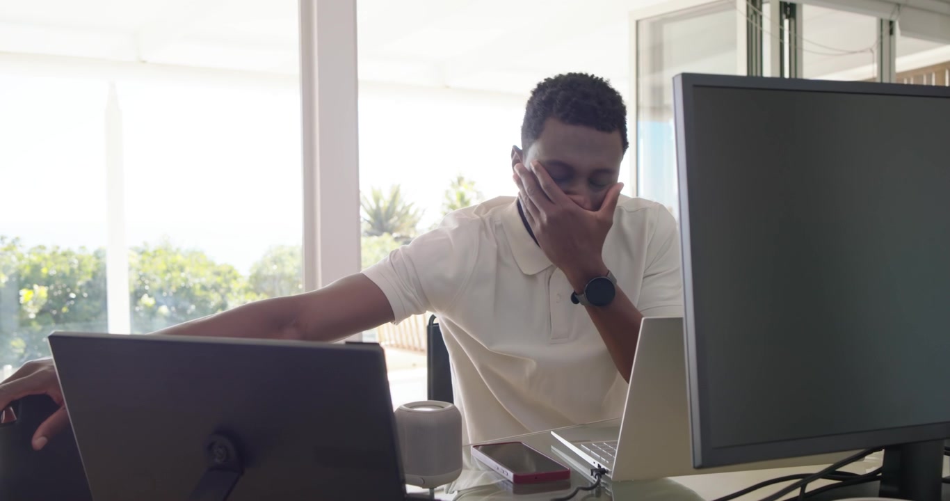 African American man in 30s at home office, seeing doc on laptop, typing and adjusting monitors
