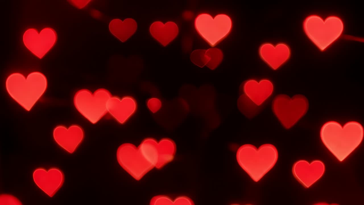 Bokeh a forma di cuore rosso raggruppati che si muovono verso il centro sovrapponendosi su uno sfondo scuro, con cambio di messa a fuoco