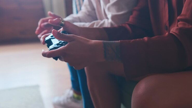 Woman hands using joystick playing video game sits on sofa in living room
