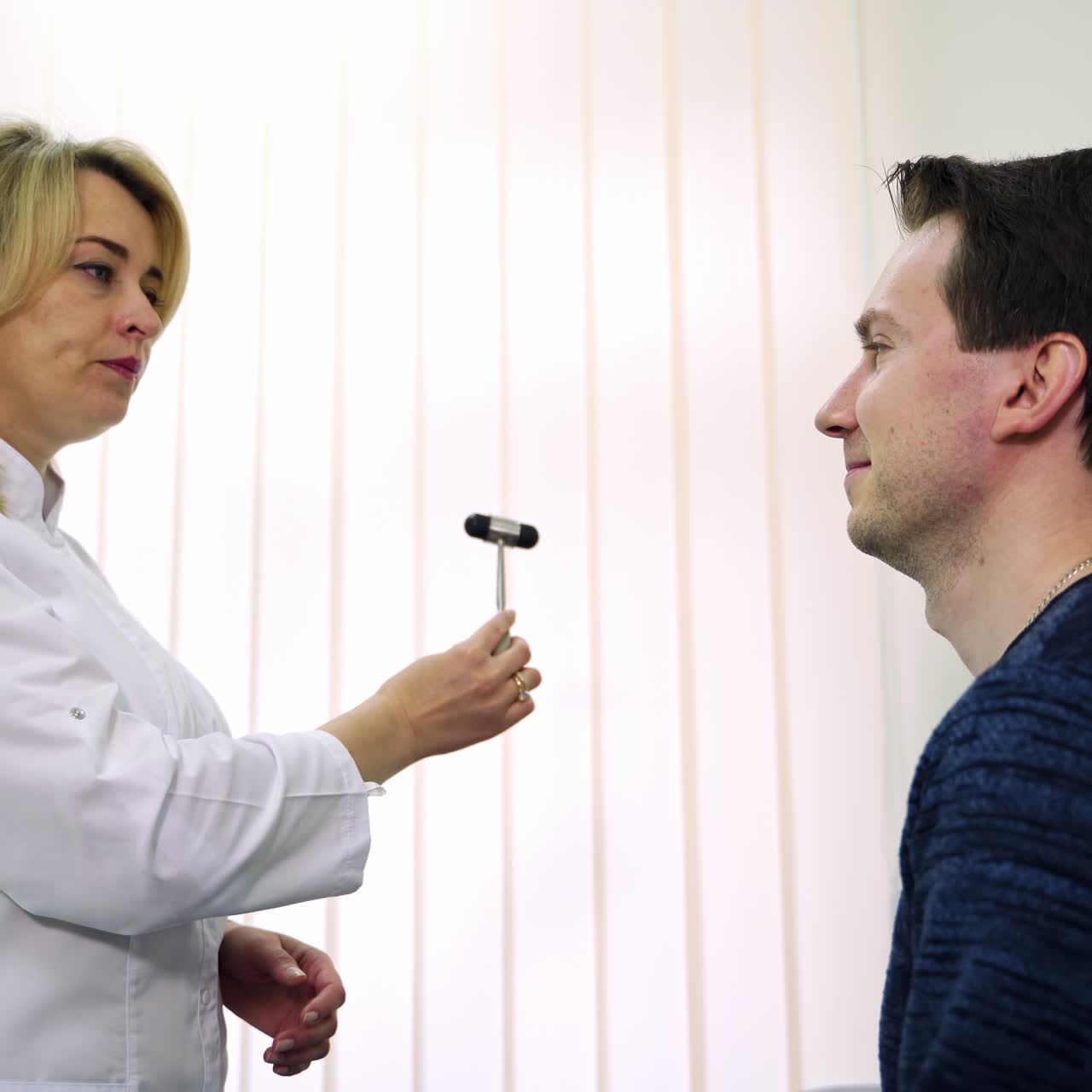 Neurologist checking the male patient's reflexes. Female medic showing the little hammer to a man asking him to follow it with sight. Side view