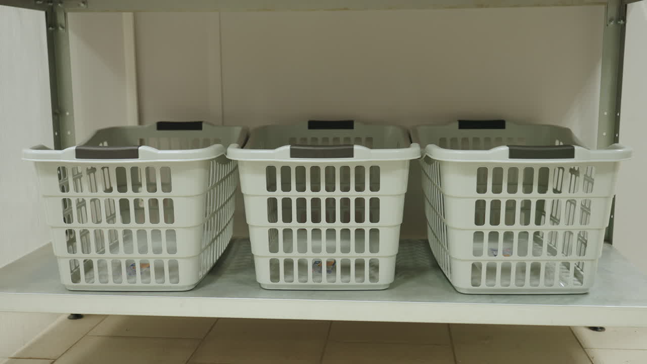 Inquadratura ravvicinata di cesti portabiancheria in plastica posizionati ordinatamente su un ripiano metallico all'interno di una lavanderia. I cesti vuoti sono allineati in fila e pronti per l'uso, mettendo in evidenza il sistema di stoccaggio utile in un impianto di pulizia organizzato