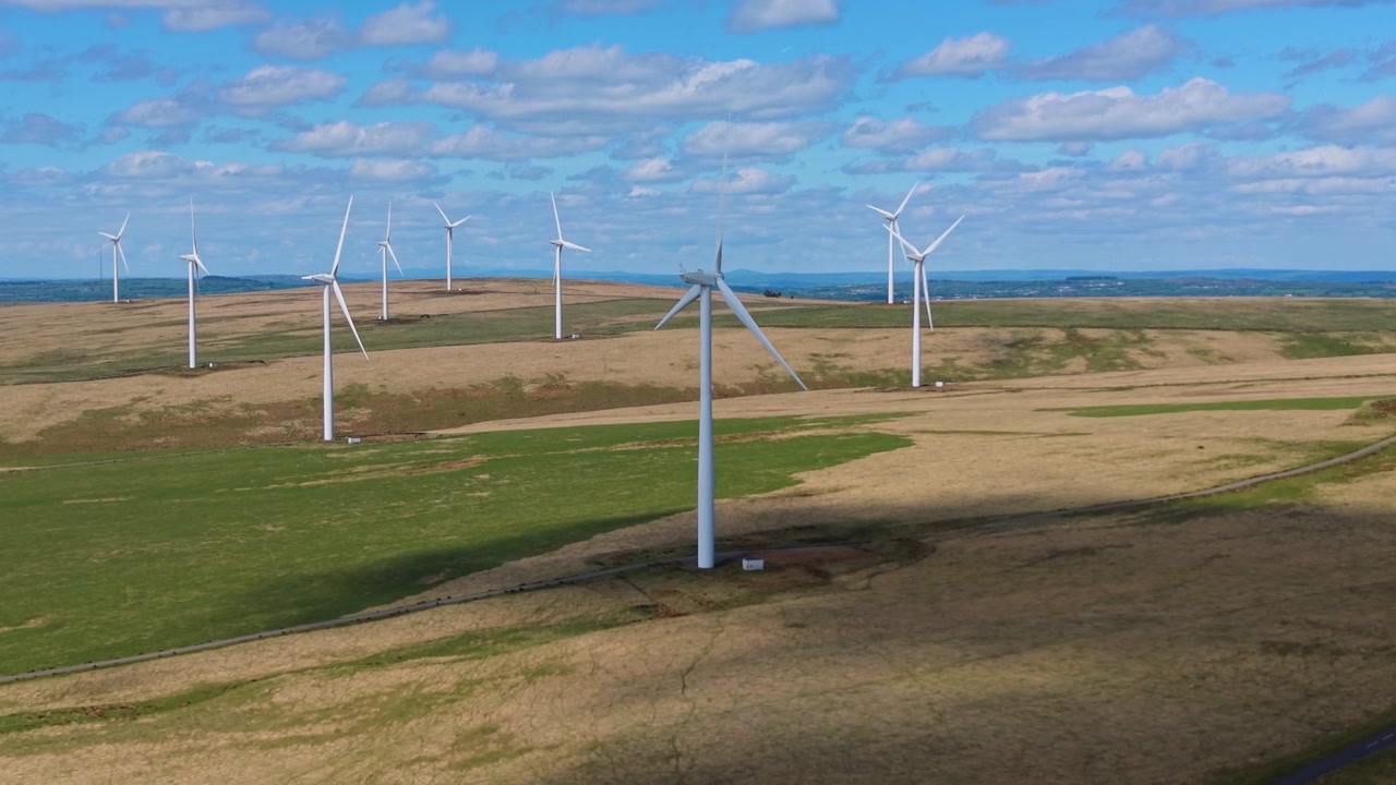 Large Wind Farm in Wales with Dramatic Landscape and Colorful Blue Sky. Aerial Drone Clip of Renewable Energy Generation Infrastructure in UK. 4K.