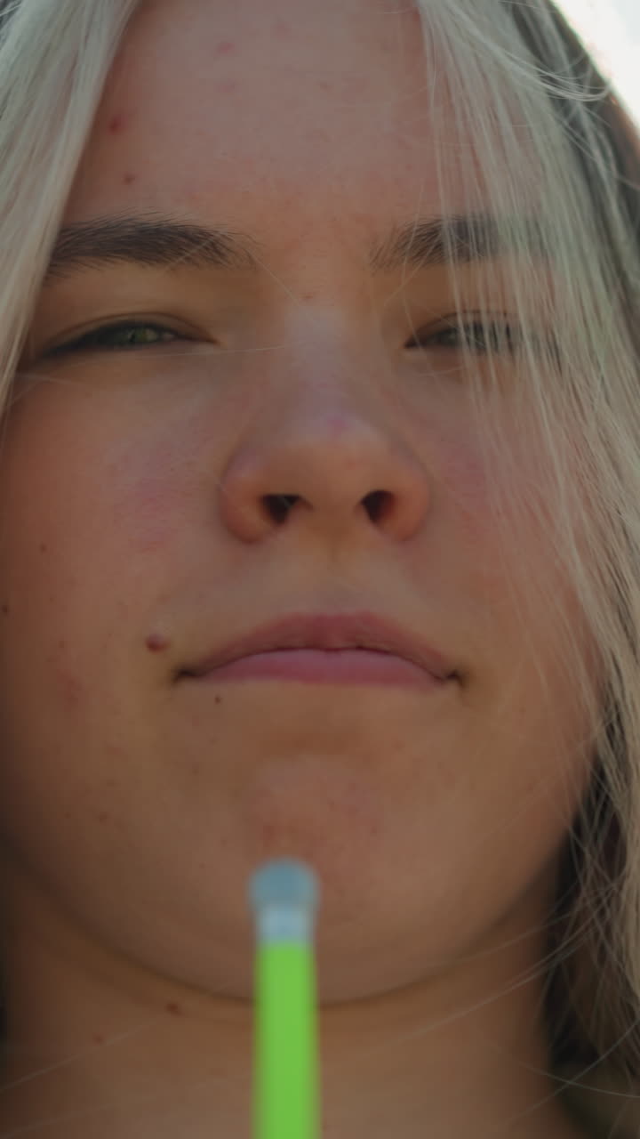 primer plano de una mujer joven de pie a la luz del sol, usando una bomba de aire verde para enfriar su cara mientras cierra los ojos ligeramente, sintiendo una suave brisa en su cara, la luz solar se filtra a través