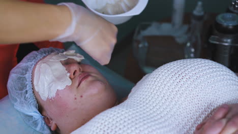 beautician applies alginate mask onto plus-size woman face