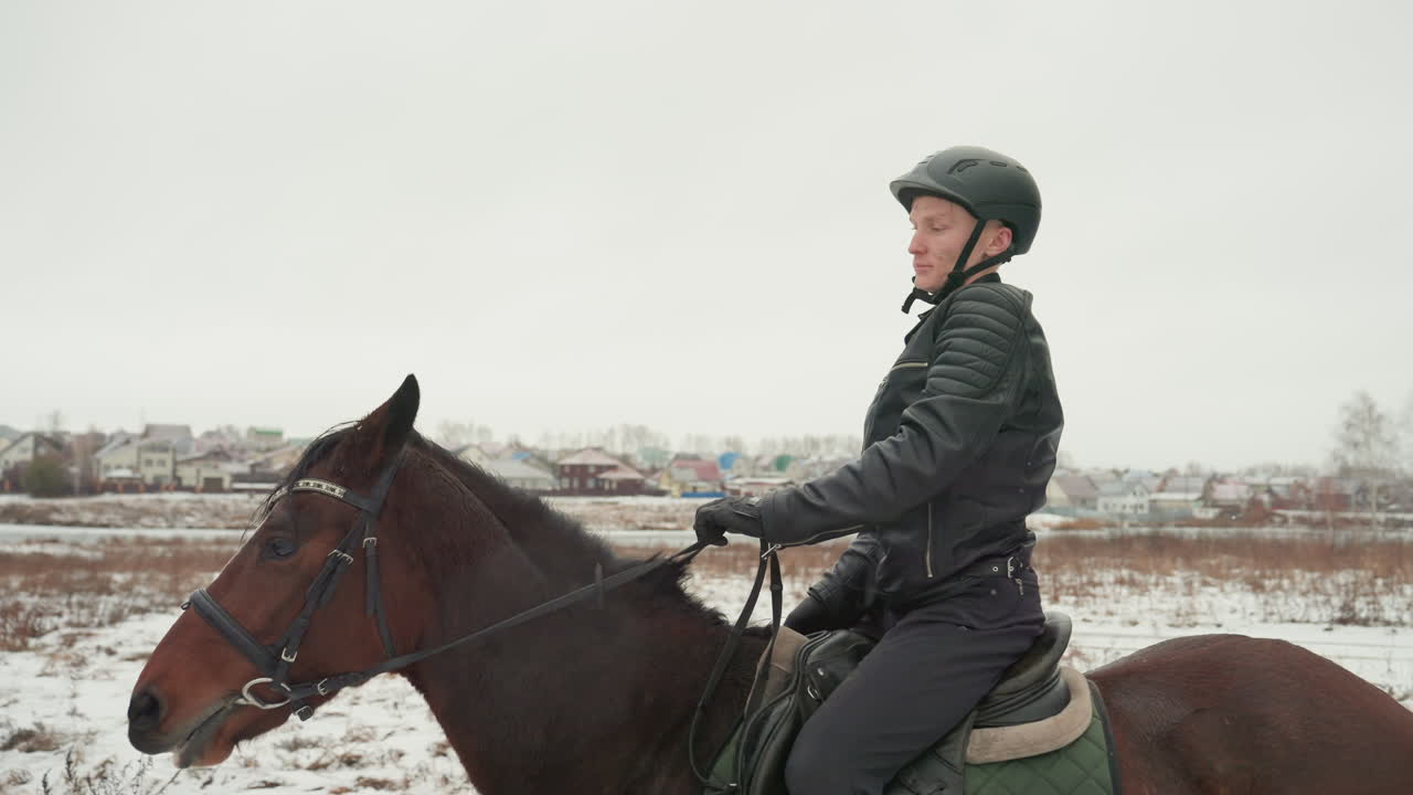 Белый всадник садится на лошадь в снегу. Белый всадник в шлеме садится на коричневую лошадь на заснеженном поле во время парного обучающего занятия, отрабатывая безопасную технику посадки и сбалансированную позу, зеленый вальтрап