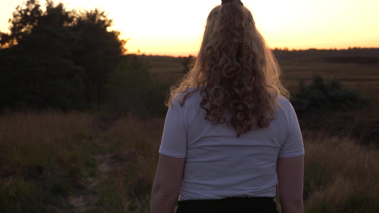 Young blonde girl plays with her hair and walks straight to the beautiful sunset, golden hour, nature, slow motion