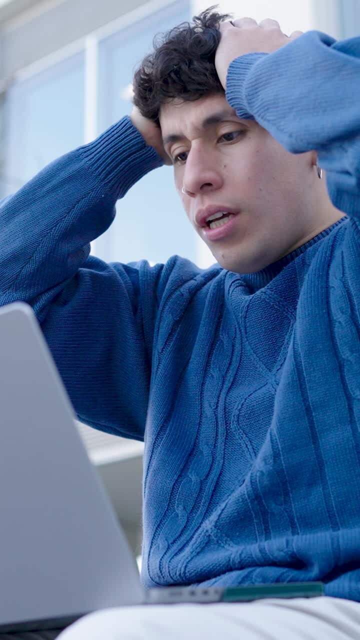 Young hispanic student reacting with surprise and frustration while working on laptop. Vertical