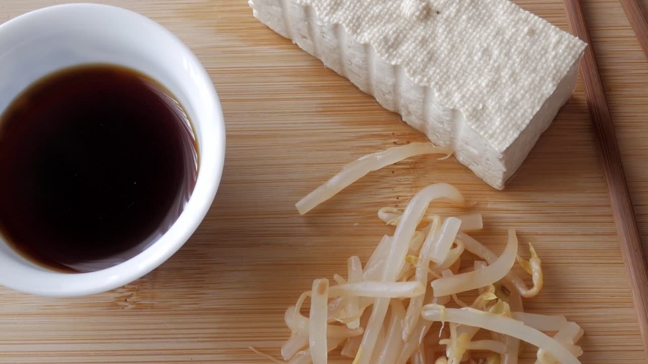 Tofu block with bean sprouts and soy sauce on wooden board, minimal cooking prep