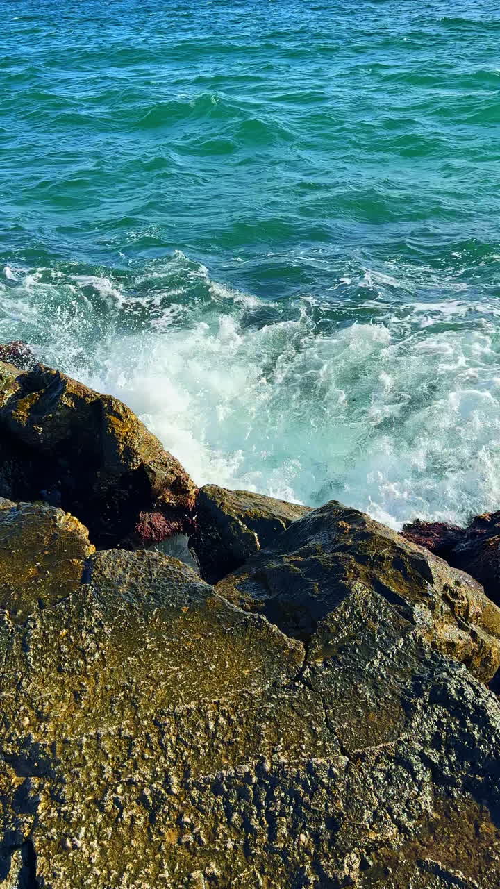Le onde si infrangono contro le rocce sulla riva dell'oceano in una giornata di sole con cielo azzurro e limpido
