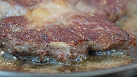 detailed closeup of entrecote frying in butter, showing the seared crust and sizzling edge in the pan