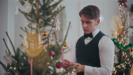 young man in tuxedo decorating christmas tree at home