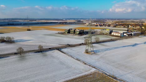 Aerial-Winter-View-of-Countryside-with-Snow-Dusted-Fields-and-Electrical-Tower