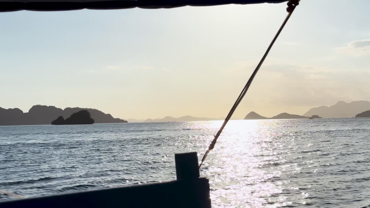 POV view from a boat on a trip sailing around Palawan in The Philippines. You can see the sun shining off the calm ocean and the islands and mountains in the background.