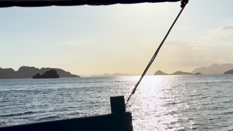pov view from a boat on a trip sailing around palawan in the philippines. you can see the sun shining off the calm ocean and the islands and mountains in the background.