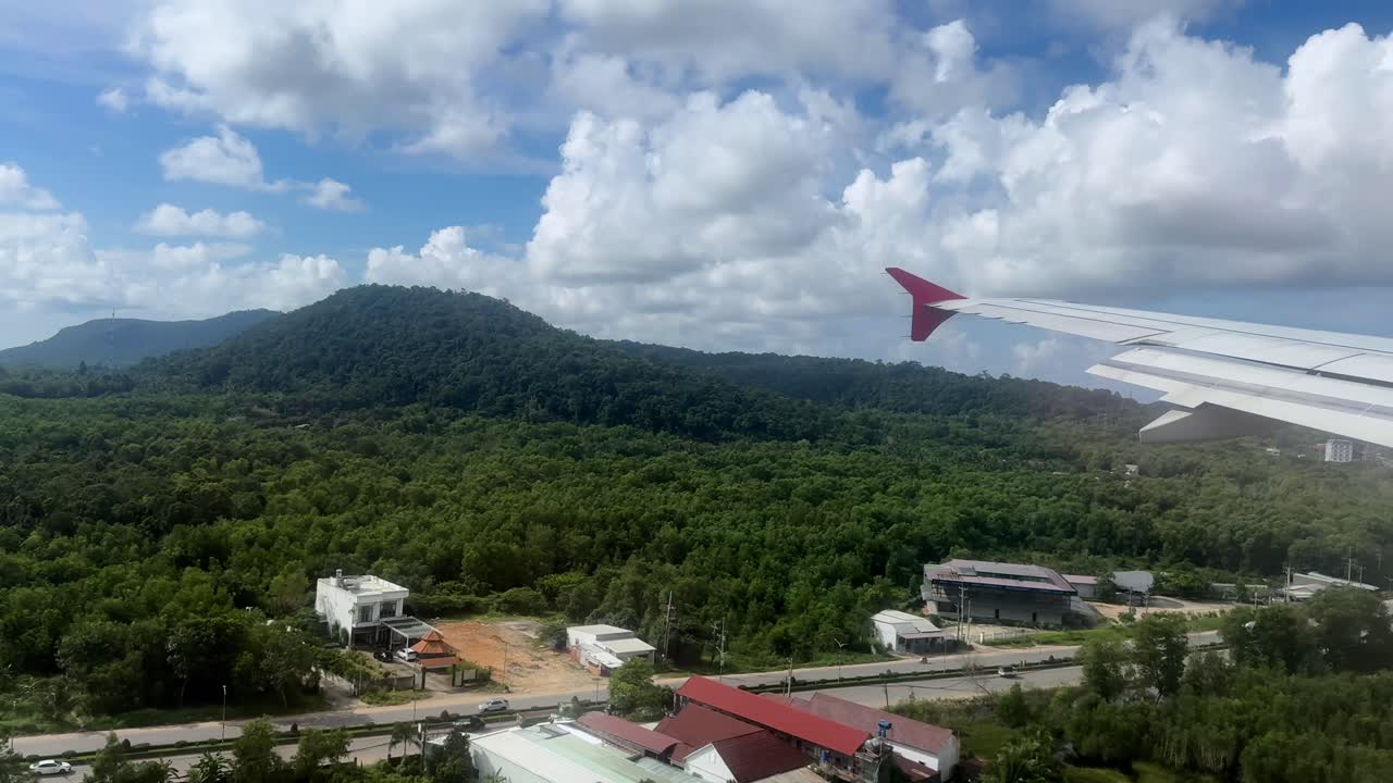 Airplane flying over lush forest with hills under cloudy sky