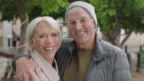 Retrato-De-Una-Feliz-Pareja-De-Ancianos-Caucásicos-Sonriendo-Alegre-Abrazando-Mirando-La-Cámara-Viejo-Matrimonio-En-La-Ciudad