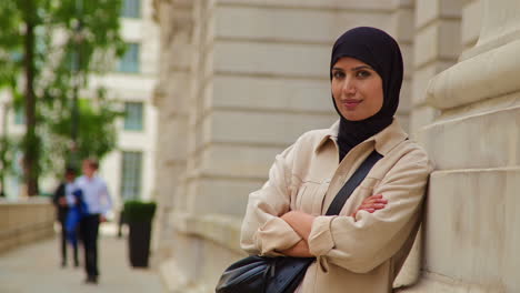 portrait of smiling muslim businesswoman wearing hijab and modern business suit standing outside city office buildings