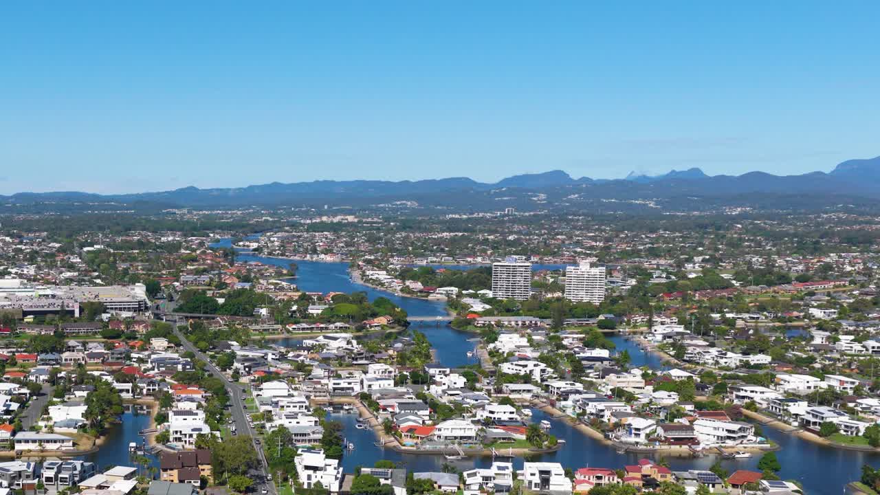 Aerial footage of Gold Coast, Australia, showcasing urban landscape, waterways, and distant mountains under clear blue skies