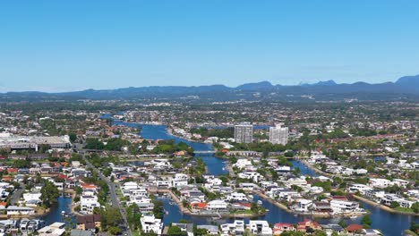 aerial footage of gold coast, australia, showcasing urban landscape, waterways, and distant mountains under clear blue skies