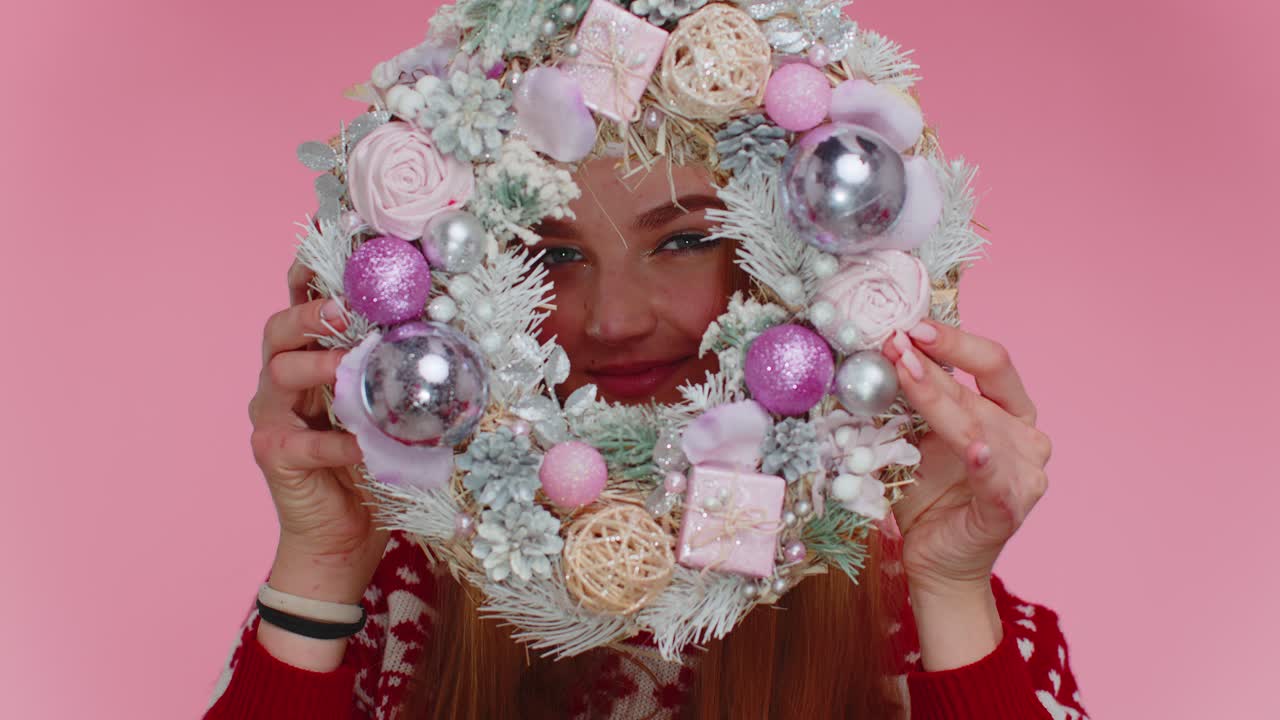 Happy woman wears red new year christmas sweater and hat hold raise festive wreath hiding behind