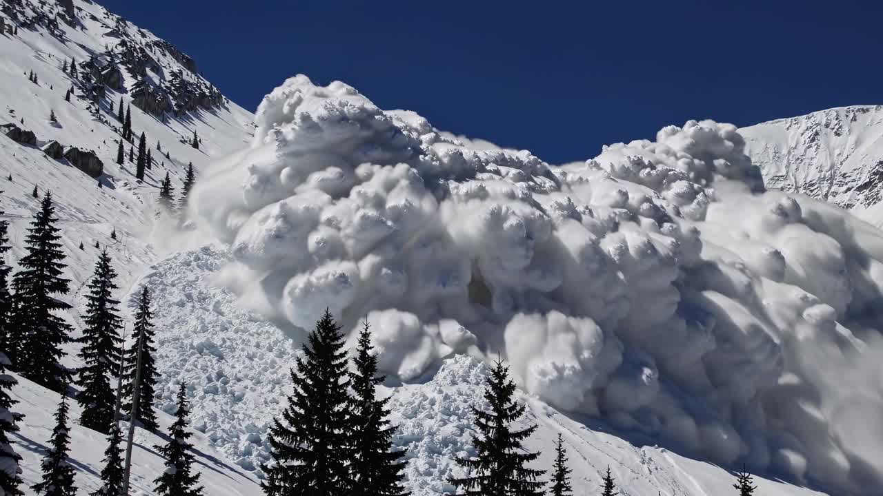 A dramatic video still of a snow avalanche captured from a low-angle, showcasing the immense power
